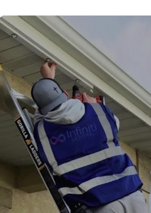 Bayline installer mounting lights under a roof edge from a ladder